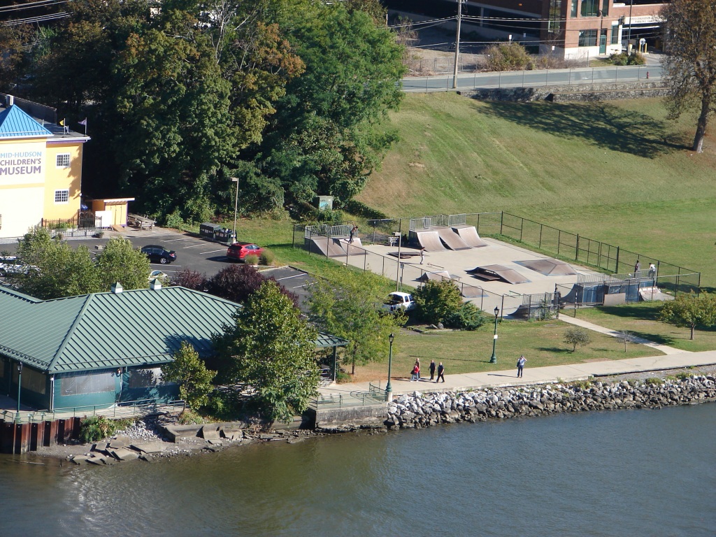 View of skate board park, children's museum and people on sidewalk next to Hudson River.
