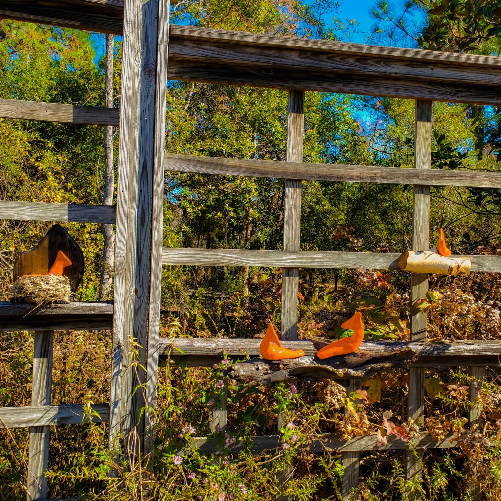 Sculptures of 4 bright red cardinals sitting on a wooden fence