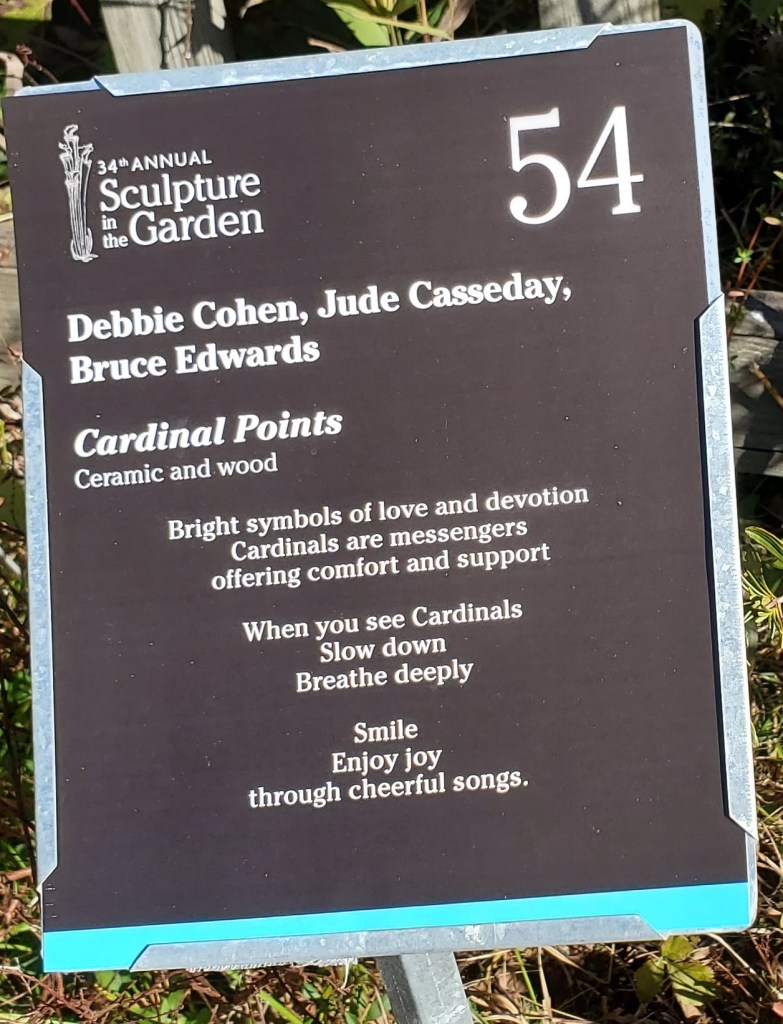 Signs that describe sculpture as ceramic and wood. QR code to scan to hear sounds of cardinals.